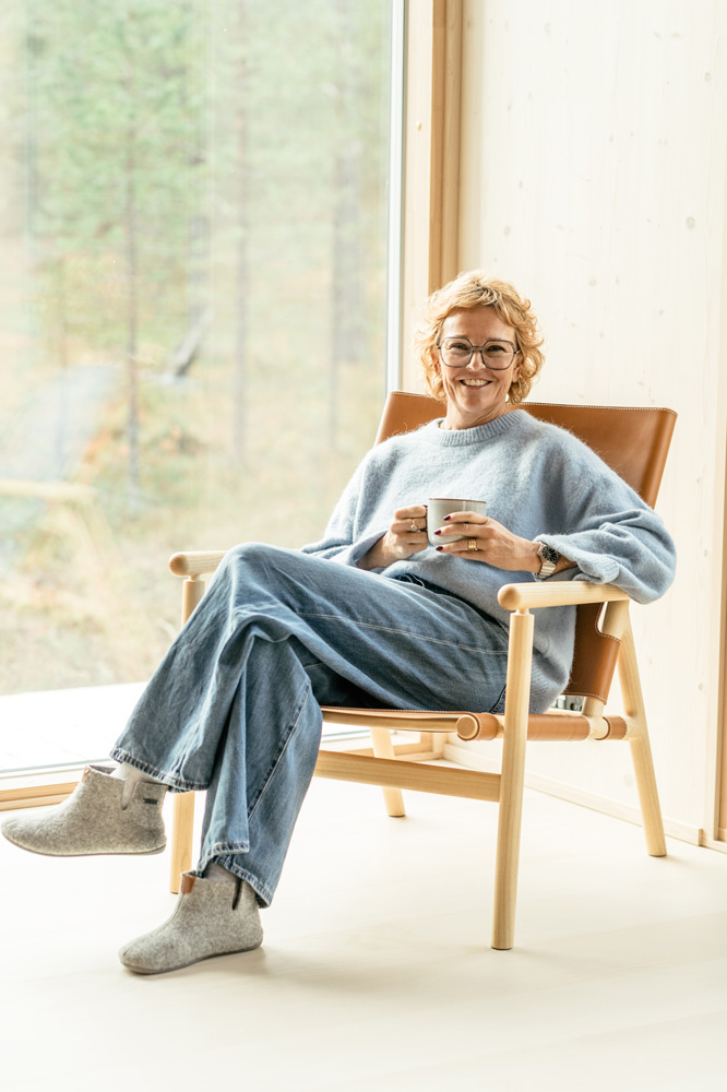 Keski-ikäinen, vaaleahiuksinen nainen istuu leveässä nahkaisessa ja puurunkoisessa Hakolan Noma-nojatuolissa ikkunan edessä ja hymyilee katsojalle. Hänellä on yllään vaaleansininen pörröinen neule, väljät farkut ja harmaat huopatossut. Hän pitää käsissään harmaata mukia. Ikkunasta näkyy metsäinen maisema.