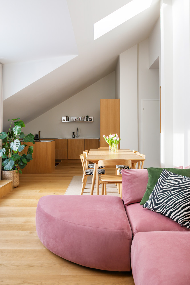 Yleiskuva valoisasta, loft-tyylisestä asunnosta, jossa on avoin olohuone, ruokailutila ja keittiö. Etualalla on vaaleanpunaisella sametilla verhoiltu Hakola Puzzle -moduulisohva, jonka L-muoto on muodostettu liittämällä sohvaan sektorin muotoinen Puzzle-kaarirahi. Sohvaa koristavat vihreä ja seeprakuvioinen koristetyyny. Olohuoneesta siirrytään ruokailutilaan, jossa on puinen ruokapöytä ja tuoleja sekä vaaleanpunaisia tulppaaneja maljakossa. Taustalla on integroiduilla puukaapeilla varustettu keittiö, joka sijaitsee vinon katon alla. Suuret ikkunat ja kattoikkuna tuovat tilaan runsaasti luonnonvaloa, joka luo pehmeitä varjoja. Vaalea puulattia yhtenäistää tilat.